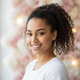A happy young woman with a high ponytail smiles confidently, against a soft background of rose, bright white, and warm cream.